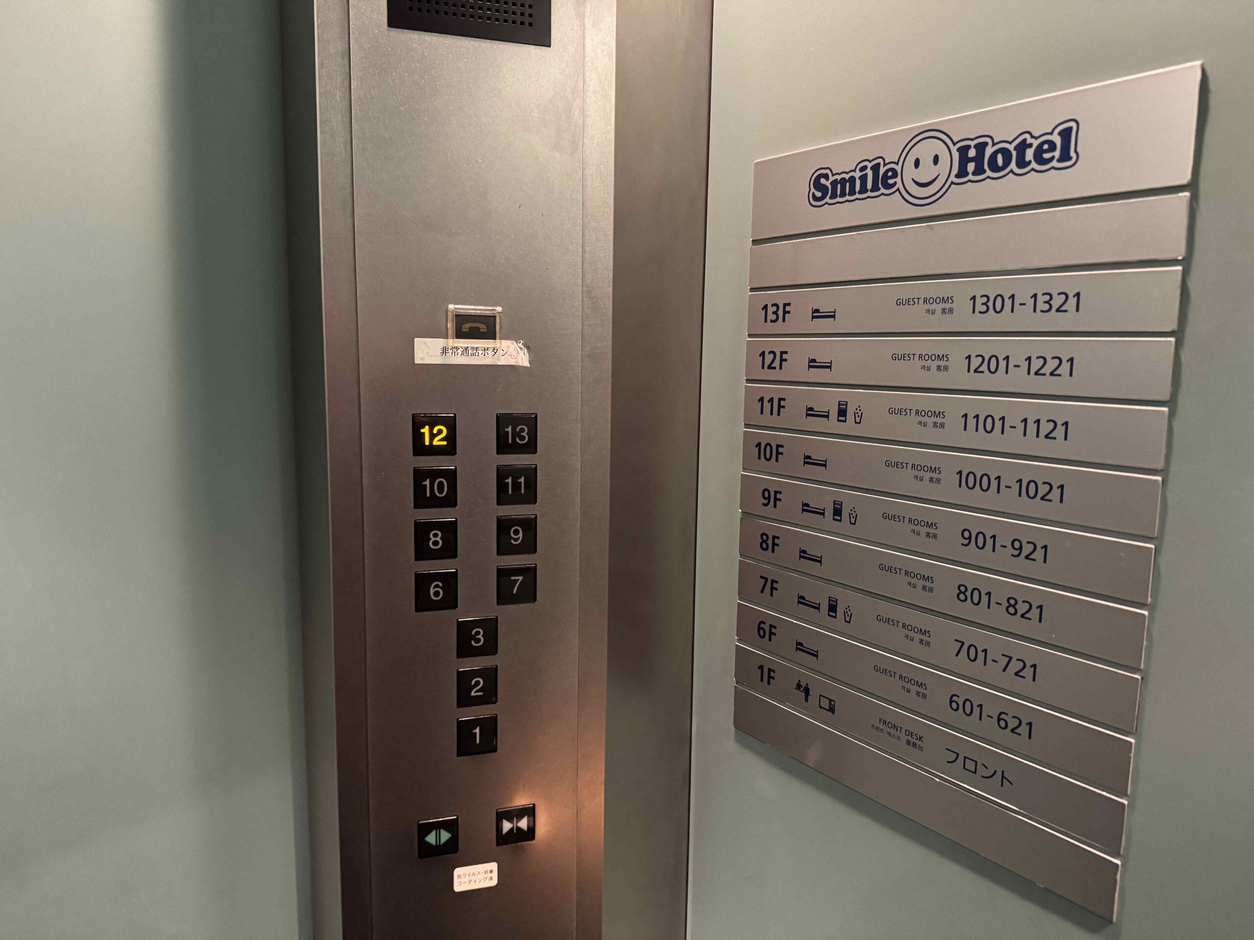 飯店電梯與樓層配置牌特寫，按鈕亮起12樓位置，旁邊看板顯示Smile Hotel六樓到十三樓客房分布