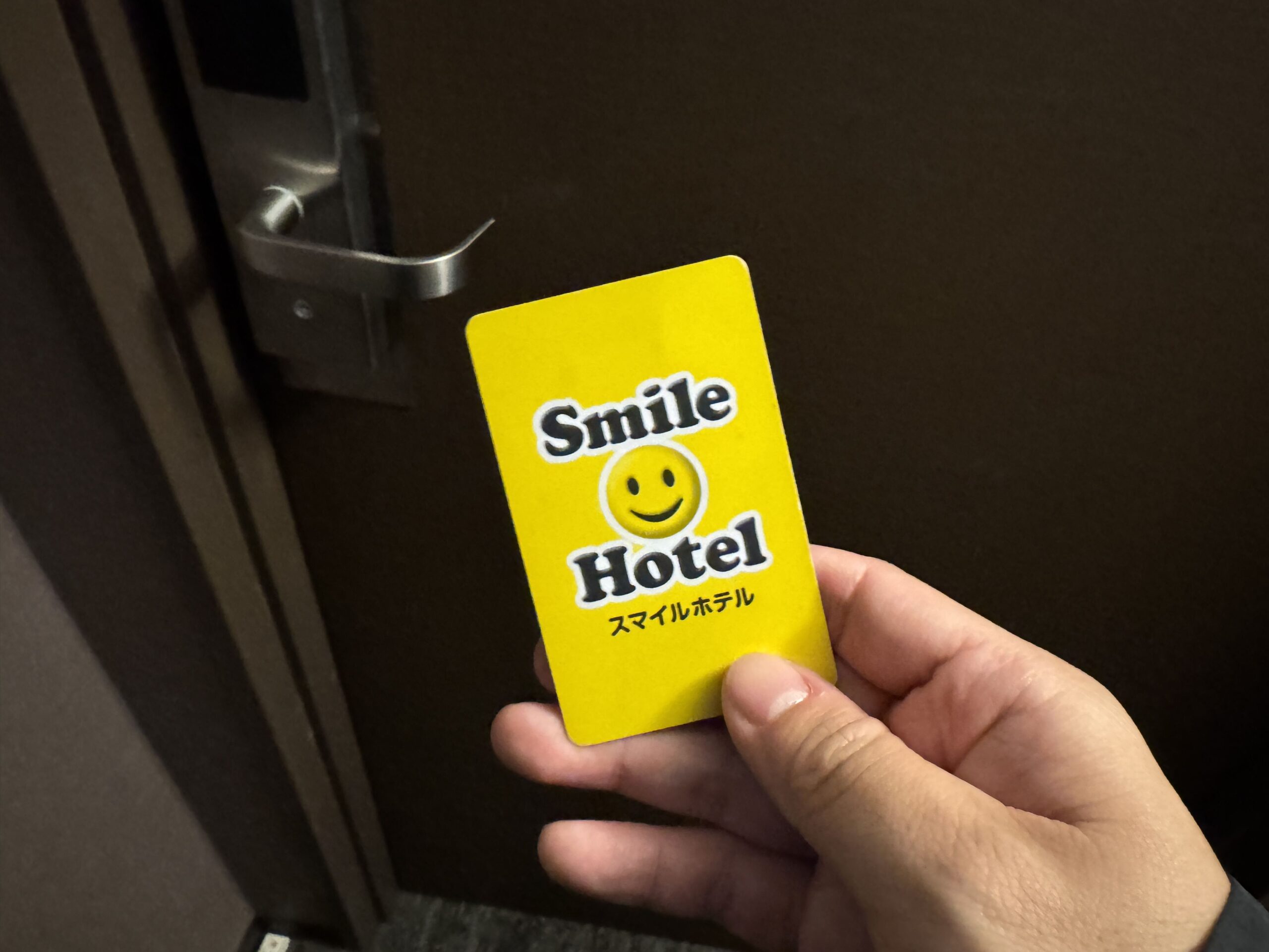 大阪微笑飯店黃色卡片式房卡，正面印有Smile Hotel品牌logo與微笑表情，スマイルホテル日文標示