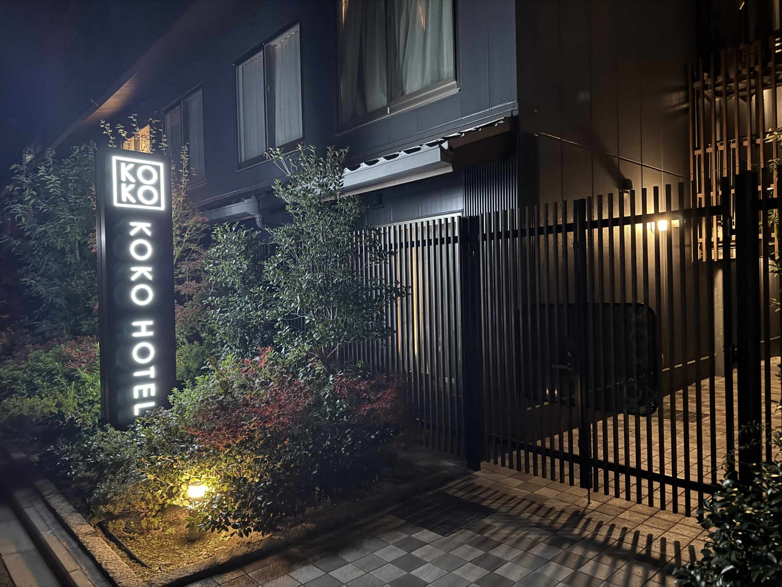 KOKO HOTEL京都三條飯店直立燈箱招牌，夜晚燈光打亮黑色立面與綠色植栽