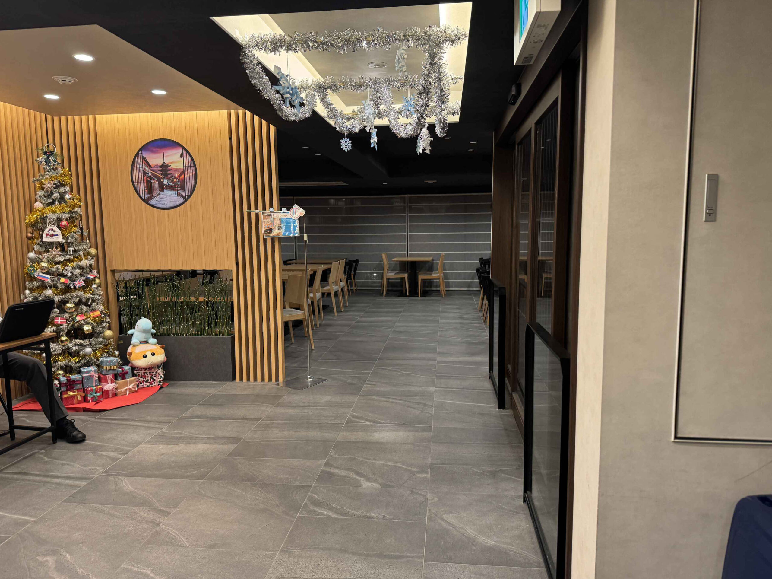 12月聖誕氛圍下的大廳，銀色鈴鐺燈飾從天花板垂下、聖誕樹擺在牆角、京都地圖鐘掛牆與耶誕老人玩偶